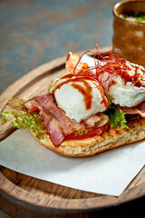 Sandwich with tomato, bacon and poached egg on white bread. Concrete background. Eggs Benedict for breakfast. Morning light with hard shadows