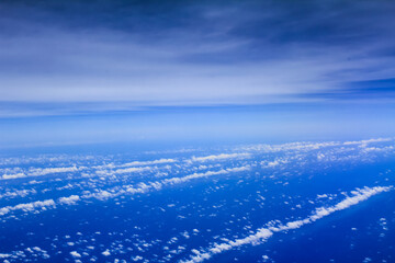 Cloudscape background. View from above, out of an airplane window. Different shades of blue in the sky.