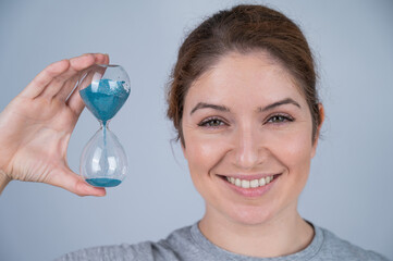 Caucasian red-haired woman holding an hourglass on a white background. Aging concept.