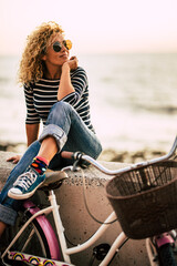 Pretty woman sitting outdoor with a bike having relax leisure activity with beach in background. One female people healthy rider lifestyle. Transport and sustainability environment. Happiness freedom