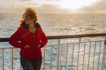 Cruise ship vacation woman enjoying sunset on travel at sea. Traveler happy woman in red jacket...