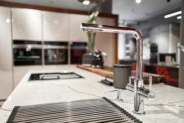 Stylish metallic crane at the kitchen. Sink faucet at the kitchen. Metal crane in close-up photo. Details of the interior of the kitchen in the house. - 568890328
