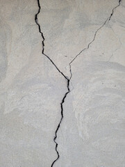 Cracked concrete wall covered with gray cement mortar. Destruction caused by an earthquake. Vertical uneven crack in the wall. Copy space. Texture background