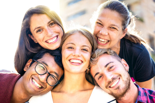 Multicultural guys and girls taking selfie out side with backlight - Happy milenial life style concept on young diverse friends having fun day together - Bright warm filter with sunshine flare