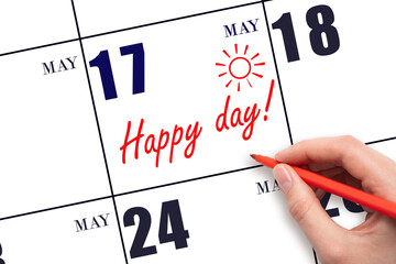 Hand writing the text HAPPY DAY and drawing the sun on the calendar date May 17