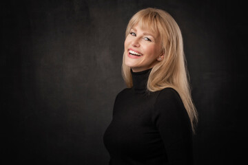 Fototapeta premium Studio portrait of blond haired woman standing at isolated dark background