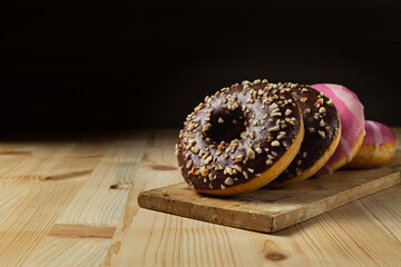 Donuts with chocolate and pink frosting over a wooden table and dark background