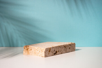 Travertine podium for presentation cosmetic products on blue background. Palm leaves shadow.