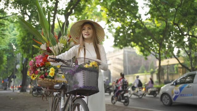 Portrait of Asian peddler with bike and flowers, Vietnamese woman girl traveling in Hanoi urban city town, Vietnam. People lifestyle.