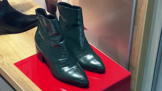 Women's high-heels dark green leather boots stand in the shoe store window
