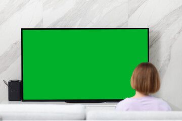 Woman sitting on the couch and watching tv. Green screen concept	