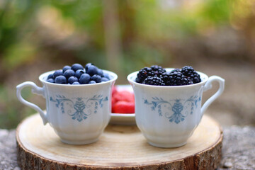 Blueberries, blackberries and strawberries in the vintage porcelain set. Healthy snack served in a garden. Selective focus.