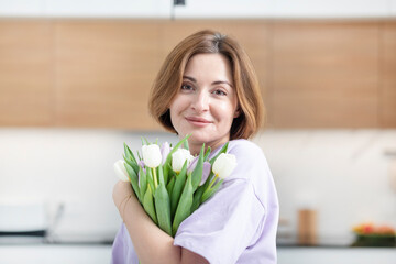 Young beautiful and happy woman standing in the kitchen with a bouquet of flowers	