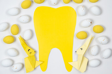 Easter and dentistry - tooth and hares made of paper, origami and yellow and white eggs, top view