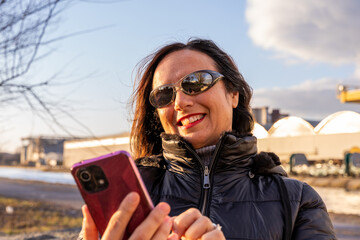 middle aged woman wearing winter clothes using smartphone in front of a factory
