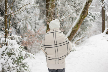 Portrait of young woman in warm clothes in winter forest. Drinking hot tea outdoors from thermos. Hiking. Tourism.