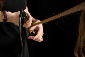 hands of hair stylist close up prepares woman makes curls hairstyle with curling iron. Long light brown natural hair.