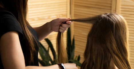 Hair stylist prepares woman makes curls hairstyle with curling iron in a beauty salon. Long light brown natural hair.
