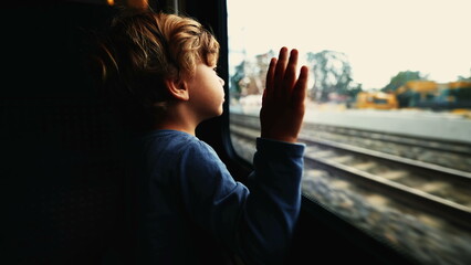 Dreamy clip of a Child leaning on train window looking at landscape passing by. Young boy daydreaming. Kid traveling