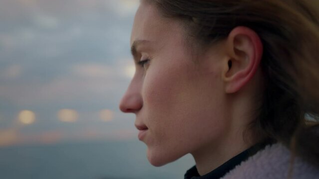 cinematic profile closeup shot of a young attractive woman looking at the sea or ocean during sunrise being in romantic mood. early morning sky and windy weather. wind blows hair