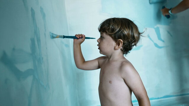 Child Paints Wall With Paintbrush. Cute Small Boy Helping Mother With House Renovation. Kid And Parent Painting Home Wall