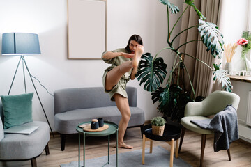 Sportswoman doing high kick in living room at home