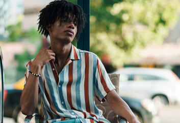 joven afroamericano posando y sentado en la ciudad en un día soleado con una camisa con líneas de...