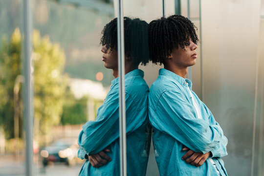 retrato de hombre negro guapo esperando en un vidrio con su reflejo en la ciudad, triste y melanc&oacute;lico.