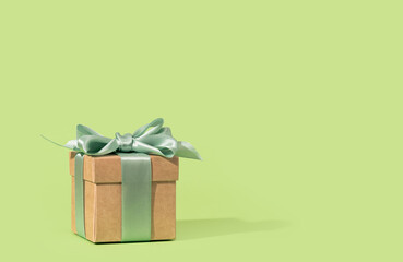 Buff paper gift box with green ribbon bow on soft green background. Gift or holiday concept....