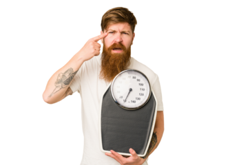 Adult redhead man with long beard holding a scale isolated cut out showing a disappointment gesture with forefinger.