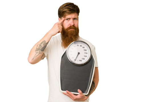 Adult redhead man with long beard holding a scale isolated cut out pointing temple with finger, thinking, focused on a task.