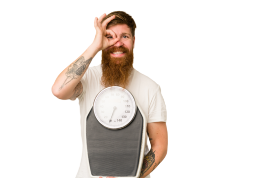 Adult redhead man with long beard holding a scale isolated cut out excited keeping ok gesture on eye.