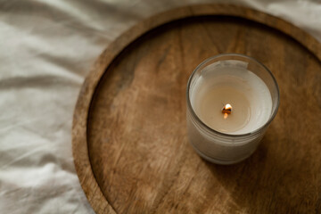 Burning candle on a wooden tray on the bed. Cozy house. Decor, details.