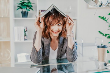 Woman book on her head. Surprised happy brunette in a jacket with a book on her head looks away...