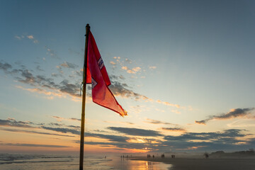Red flag by the sea with sunset background.