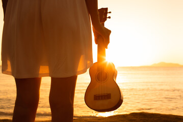 Happiness and peace in nature. young female on the beach holding ukulele looking out to the sunset 