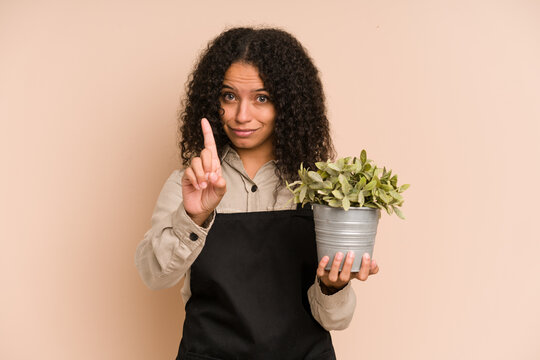 Young african american gardener woman holding a plant isolated showing number one with finger.