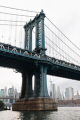 Manhattan bridge and cityscape of New York City skyscrapers under cloudy sky.