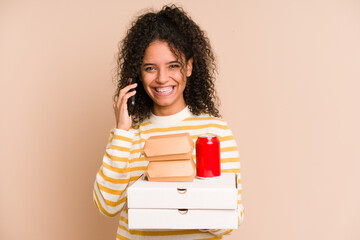 Young african american woman holding a pizza and burger fast food calling with mobile phone isolated