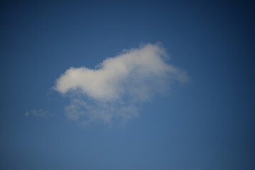 rays of the sun through the cirrus clouds against the blue sky, white rainy clouds blue sky illuminated by the rays of the sun, one small cirrus cloud blurred clouds background