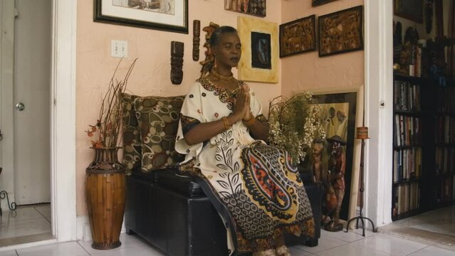 Black Stock Footage of happy, spiritual, and creative elderly Black African senior woman in her afro-centric home filled with African artifacts, art, and sculptures dancing and expressing herself