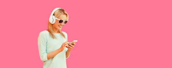 Portrait of happy smiling young woman in headphones listening to music with smartphone on pink...