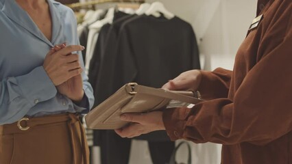 Cropped shot of shop assistant offering elegant leather bag to customer in designer boutique