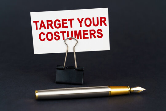On the black surface is a pen, an office paper clip with a business card on which is written - Target Your Costumers