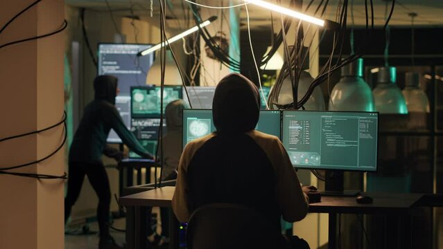 Male web criminal committing cyber crime with network malware, using trojan virus to break into computer server. Skilled hacker practicing espionage and cryptojacking. Tripod shot.