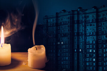 Burning flame and extinguished candle and night multi-storey building with dark windows on...