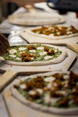 Prepared uncooked raw making pizza plant-based, with tomato pesto and white ricotta sauce and vegetables on a board, Male hands close up of placing ingredients making process. 