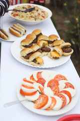 platter of sliders and platter of caprese salad on white platters at summer barbecue 