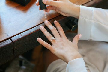 closeup of bride with engagement ring painting her nails with pale pink polish