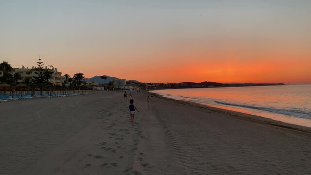 Ni&ntilde;o peque&ntilde;o corre sobre la arena de la playa en un amanecer